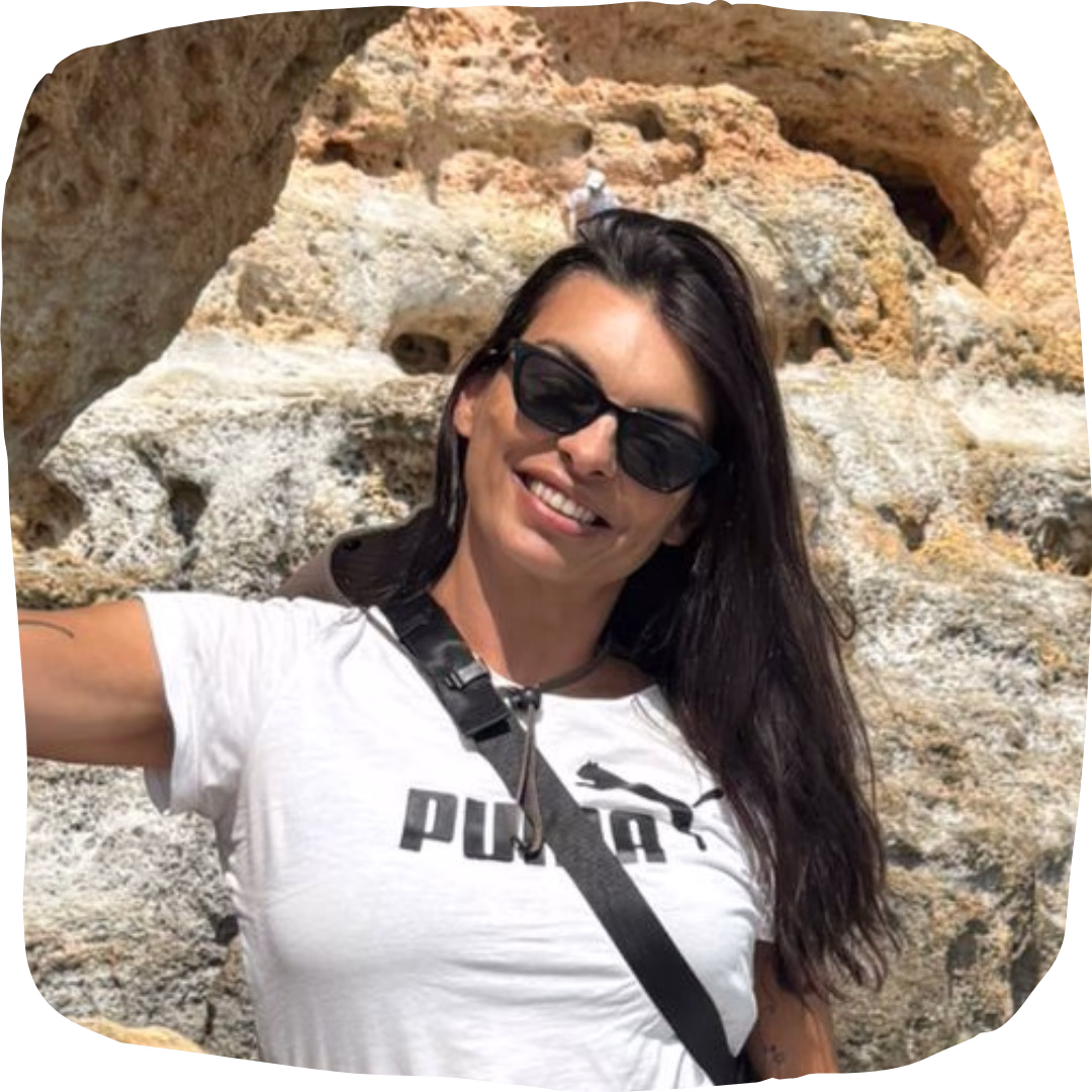 Smiling tour guide wearing sunglasses by the rocky cliffs of the Algarve, welcoming travellers on our Algarve coast tour from Faro.