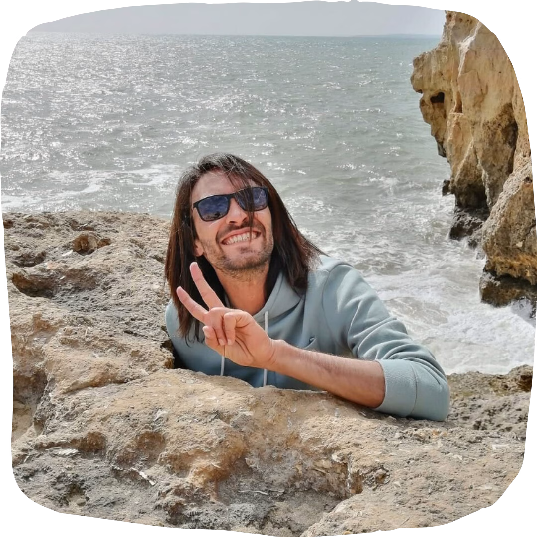 Smiling tour guide making a peace sign by the rocky Algarve cliffs and ocean, welcoming travellers on our Algarve coast tour from Faro.